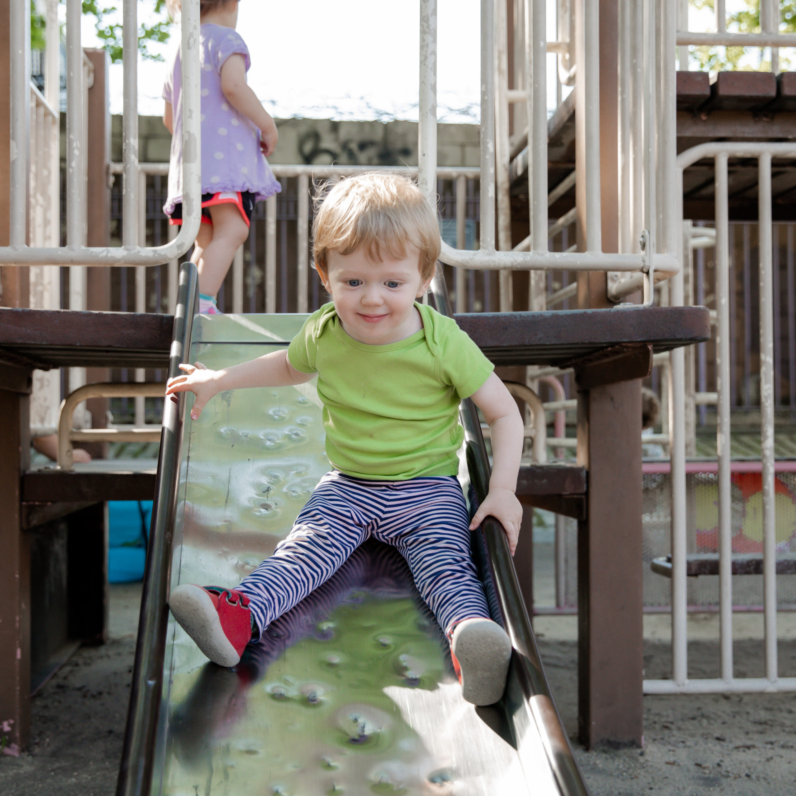 A little boy riding down the slide at a playground.