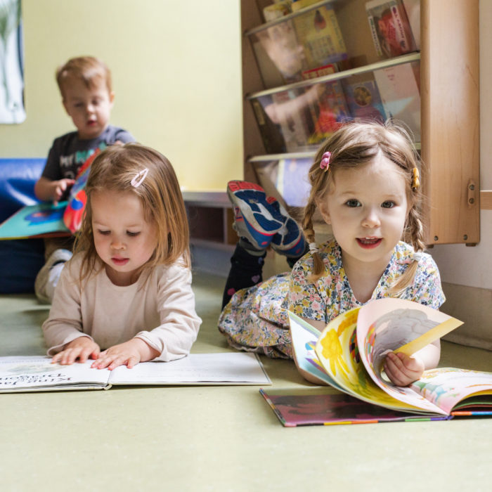 Three children are sitting on the floor reading books.