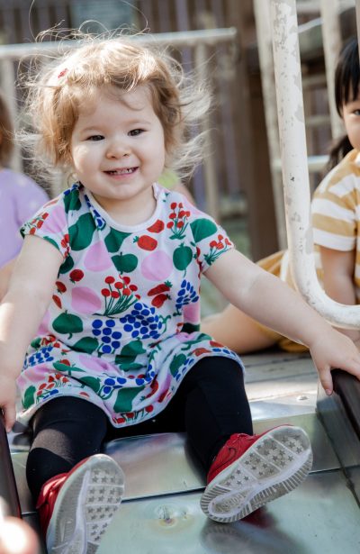 A little girl sitting on top of a slide.